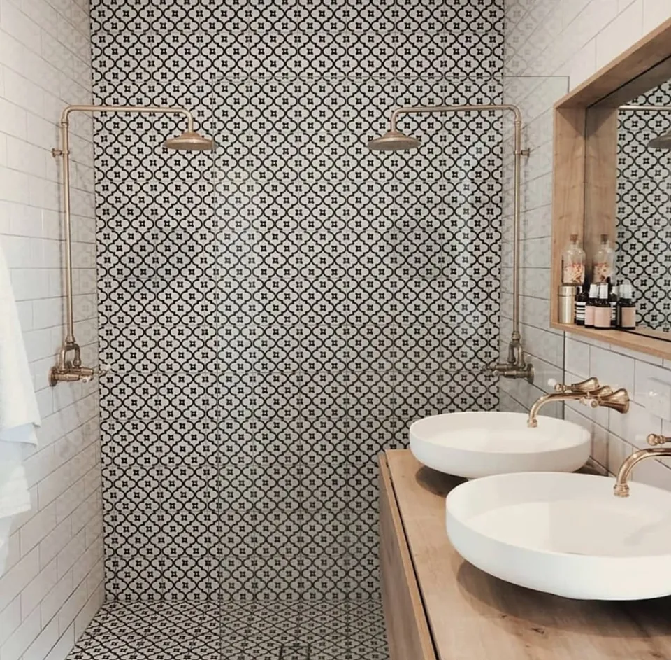 Baño con ducha doble, azulejo hidráulico en blanco y negro y lavabos sobre encimera de madera