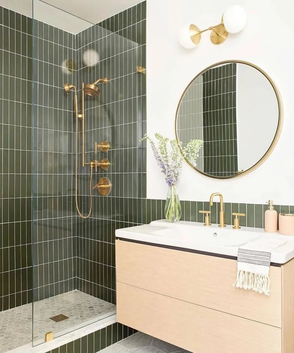 Baño con azulejo verde, grifería de latón y mueble de madera clara