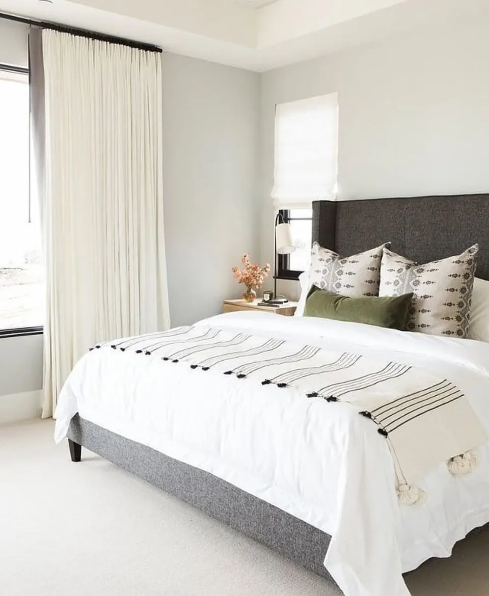 Dormitorio principal luminoso con cabecero tapizado gris y textiles en blanco